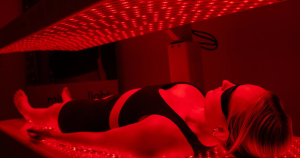 A woman lays in a red light therapy bed.